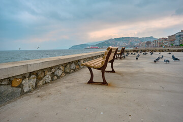 28.02.2021. Bursa turkey. Mudanya bursa during overcast weather and cloudy day with street bench exposed to corrosion metal side of bench with doves and pigeons concrete ground.