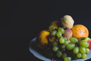 FRUITS, Sweets, tropical fruits, fruits grown in South America. small green grapes, granadilla, apple and peach. plate with fruits on black background. winery photography, product photography style.