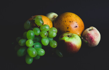 FRUITS, Sweets, tropical fruits, fruits grown in South America. small green grapes, granadilla, apple and peach. plate with fruits on black background. winery photography, product photography style.