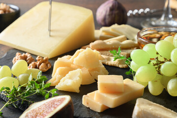 Cheese platter with grapes, nuts, figs on black slate plate. Close up. Festive appetizer. Party...