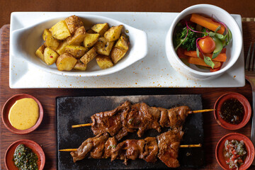 Peruvian food, meat, anticuchos, grilled on rod food, Alpaca Heart Anticucho on stone. Tourist Restaurant of Peru. Latin, South American food. with sweet potato, potato and salad.