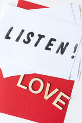 the expression "listen!" stencilled in black on white paper, with the word "love" in plain wood letters on a red background