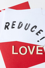 the expression "reduce!" stencilled in black on white paper, with the word "love" in plain wood letters on a red background