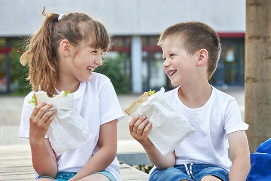 Snack during lessons. Close-up portrait of Happy children eating breakfast in the schoolyard. Meals for students during lessons