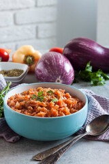 Eggplant caviar in blue bowl and fresh vegetables on background