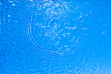 Surface of blue transparent swimming pool water texture with circles on the water. Trendy abstract nature background. Water waves in sun light reflections