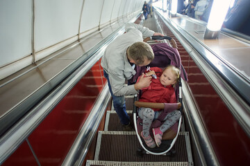 Child in perambulator with father on escalator in underground.