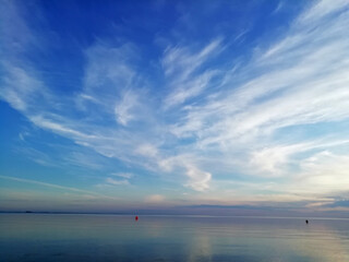 Bright azure sky, reflected in the motionless surface of the sea. The majesty and tranquility of a delightful seascape. Snow-white clouds look like a magic bird with spread wings.