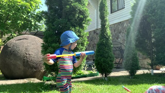 Cute Happy Kid Little Preschool Baby Girl and Boy Child Play Have Fun with Water Pump Gun Outside. Sunny Hot Nice Day in Park. Children Backyard Garden Games. Summer, Sport, Holiday, Family, Childhood