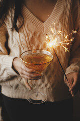 Woman holding burning sparkler and champagne glass, celebrating and toasting at party. Happy New Year! Firework bengal light and drink in woman hands. Atmospheric moment. ​Happy Holiday
