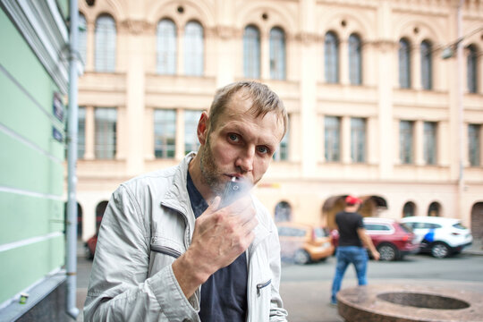 Man is smoking electronic cigarette during walking in city center.