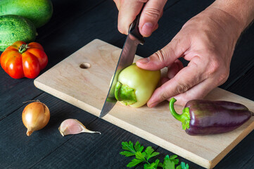 Close-up of a chef hands cuts fresh bell pepper. Cooking salad in the restaurant kitchen. Set of vegetables for a salad diet