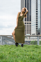 Dressing in a green Maxi Tank Dress, high heel shoes, a young fashion black girl is standing in the front of a business district and looking forward..