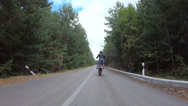 Biker stunt ride biike on mountain rural road and do wheelie on motorcycle