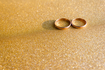 Gold wedding rings of the bride and groom on yellow glitter background. Сoncept of marriage. Copy...