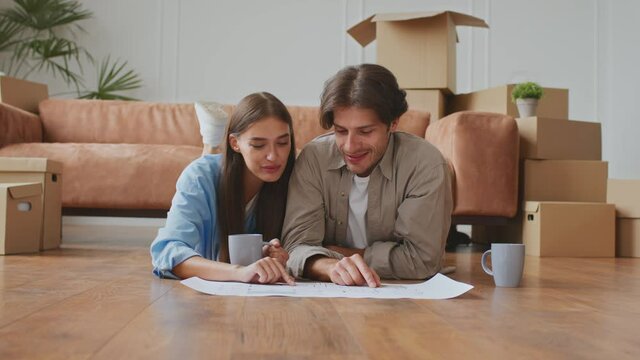 Happy homeowners. Young couple in love lying together on floor in new apartment and discussing design with plan