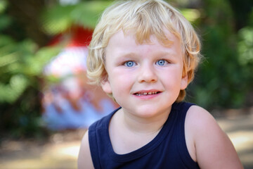 Portrait image of beautiful little blonde hair blue eyed boy in vibrant outdoor setting