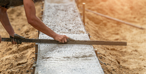Worker leveling newly poured cement into formwork with reinforcement, building foundation of residential building.