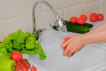 close-up of female hands washing fresh vegetables under running water in the kitchen. Tomato in hands. splashes, drops. Concept - cooking, healthy eating, vegetarianism. Horizontal photo