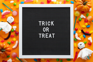Trick or treat letter board with colorful Halloween candies and decorations on orange background. Flat lay, top view, overhead. Happy Halloween concept.