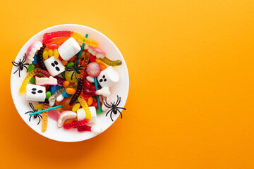 Obraz premium Halloween sweets and decorations in plate on orange background. Happy Halloween holiday concept. Flat lay, top view, copy space.