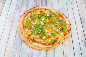 Family pizza cut into pieces with arugula sprouts, fresh cheese, pesto sauce and ripe cherry tomatoes