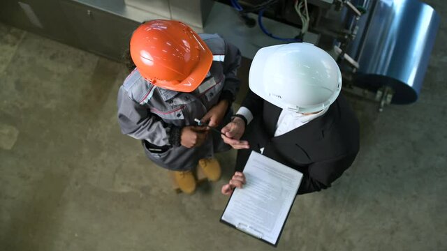 Two people in production are talking about work. Top view of white and orange industrial helmets