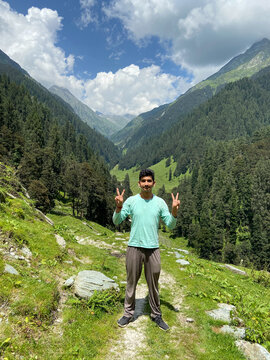 Adventurer guy giving v gesture with both hands in beautiful valley covered with grassland and himalayan cedar and fir trees