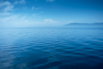 Waves on surface of water with cloudy sky and mountain. Copy space