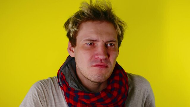 The man has a runny nose. A young guy in a scarf wipes his snot. A man has a cold, he has a runny nose. Snot flows from the nose