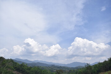 Obraz premium View of hills in the forest with a background of white clouds.