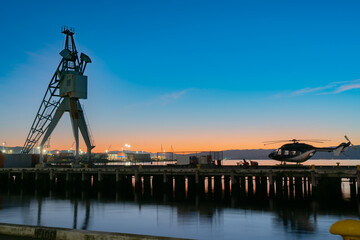 Fototapeta na wymiar Dawn across Wellington harbour from city waterfront in calm colorful long exposure landscape. with silhouette port crane and helicoptor on pier.