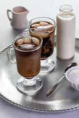 Two ice coffees served with cream and sugar, on a metal tray.