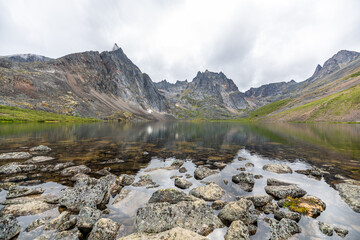 Naklejka na ściany i meble Landscape of Grizzly Lake in northern Canada, Yukon, sub arctic area with pristine water below massive mountain peaks. 