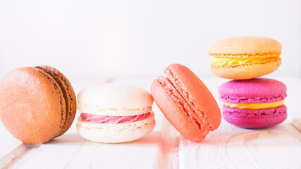Lots of multicolored macaroni cakes on white wooden background