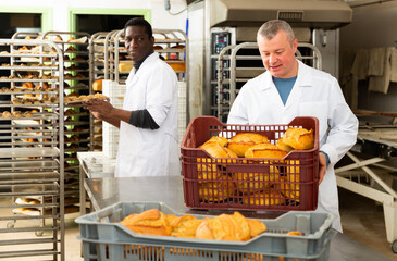 Skilled successful bakers arranging freshly baked bakery products