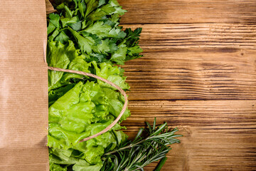 Paper bag with lettuce rosemary and parsley on a wooden table. Vegan food. Top view