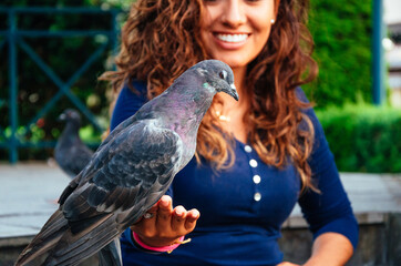 Beautiful young Latina feeding a pigeon from the palm of her hand.