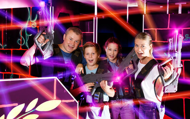 Smiling teens and theirs parents with laser guns during laser tag game indoors