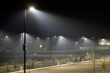 Empty parking lot at night with glowing cones of lights shining in the smoke from nearby wild fires