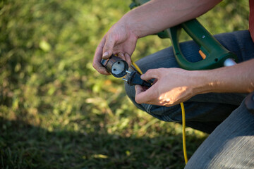 man inserts a plug from the electric trimmer into an socket outdoors - obrazy, fototapety, plakaty