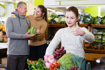 Happy little girl with loving parents choosing fresh fruits and vegetables in market