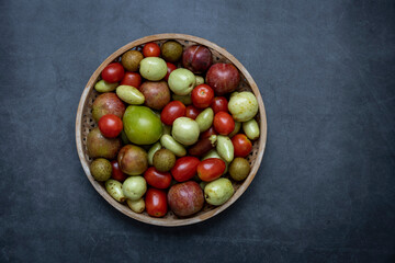 A variety of fresh fruits, dates, Cherry tomatoes, Longan, plum, are set against a dark gray background.