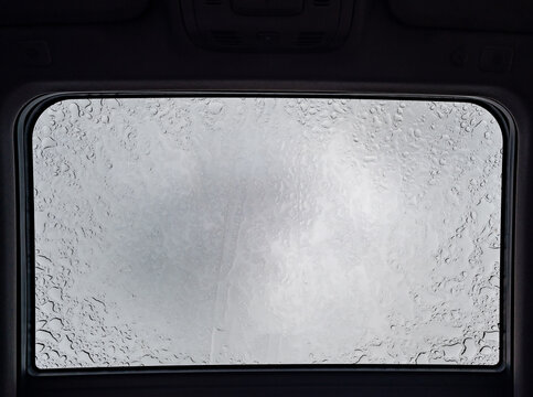 Inside a vehicle looking up to a sunroof with water droplets 