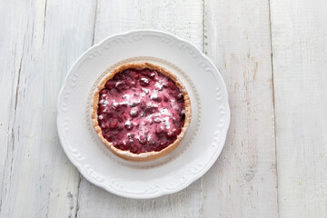 Top view of delicious sour cream tart with berries and crunchy crust served on elegant plate on white wooden table