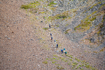 Group of hikers hiking up and over a steep mountain pass in northern Canada during summer time. 