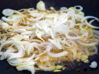 The onions are fried in a large saj frying pan outdoors. A dish for a family picnic. Ingredients for a delicious hot meal