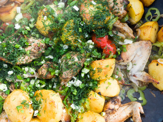 Potatoes and chicken are fried in a large Saj frying pan outdoors. A dish for a family picnic. Delicious hot food