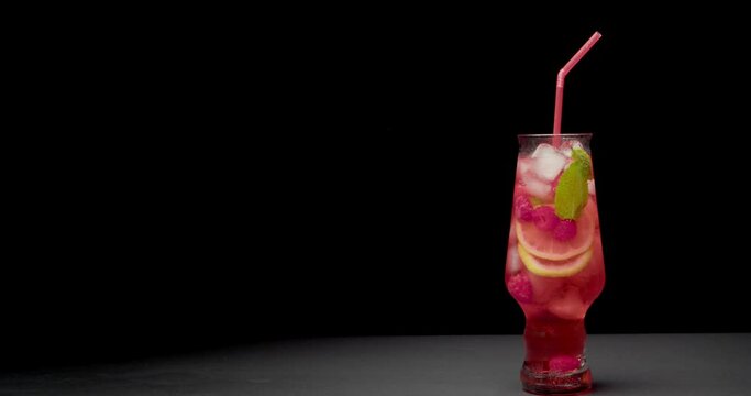 Barman putting glass of tasty raspberry lemonade on table against dark background