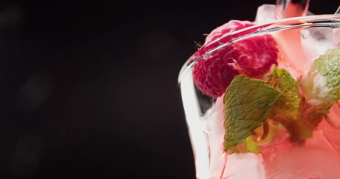 Pouring of tasty raspberry lemonade in glass on dark background, closeup